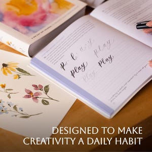 Inside view of The Daily Play showing step by step instructions of how to write calligraphy. There's a picture of watercolored flowers sitting on the table next to it.