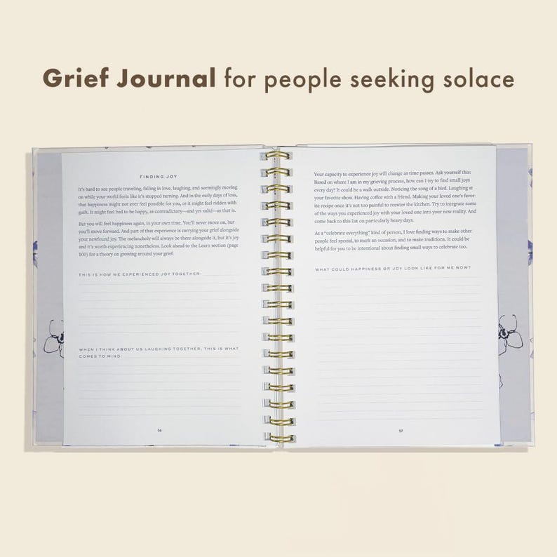Peut inclure: Journal de deuil ouvert avec une reliure &agrave; spirale dor&eacute;e. Les pages du journal sont remplies de texte et d'invites. La couverture et les pages ont un motif floral dans les tons de bleu et de violet. Le texte en haut indique "Grief Journal for people seeking solace."