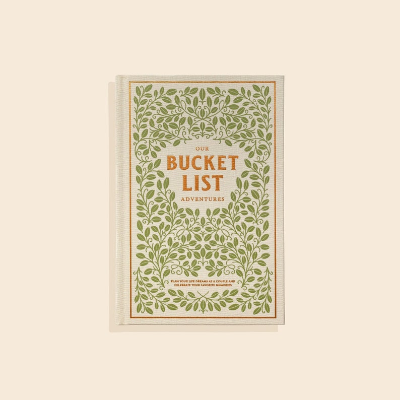 May include: Our Bucket List Adventures journal.  A cream-colored linen-textured journal cover features a copper-colored title, 'OUR BUCKET LIST ADVENTURES.'  The cover is decorated with a repeating olive-green leafy pattern.  Small copper-colored text at the bottom reads, 'Plan your life dreams as a couple and celebrate your favorite memories.'
