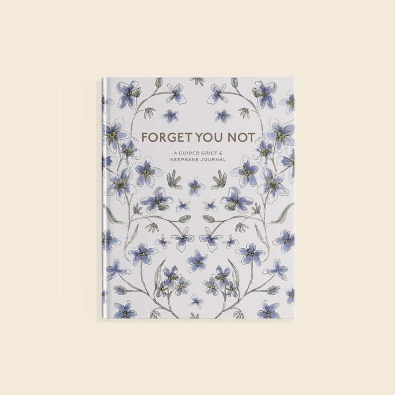 Peut inclure: Un journal &agrave; couverture rigide intitul&eacute; "Forget You Not" avec un motif floral. La couverture pr&eacute;sente un motif de fleurs bleues et de tiges vertes sur fond blanc. Le texte "A Guided Grief & Keepsake Journal" est en dessous du titre.