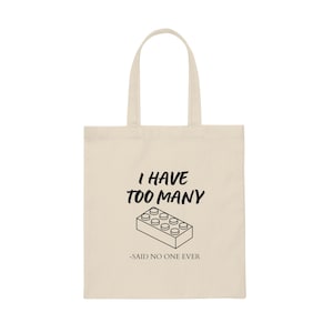 May include: A beige tote bag with a black graphic that says "I have too many -said no one ever" with a black outline of a Lego brick.