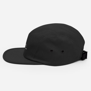 May include: A black 5-panel cap with a white embroidered design. The cap has an adjustable strap.