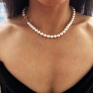 May include: A simple pearl necklace with a gold clasp. The necklace is made of white pearls and is about 18 inches long.