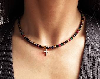 May include: A beaded necklace featuring small, round, multi-colored stones in shades of brown, blue, red, and green. The necklace is centered with a small, silver-toned cross pendant that features a vertical row of tiny, clear, sparkling stones.
