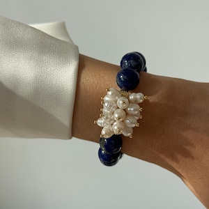 May include: A beaded bracelet featuring round, deep blue lapis lazuli stones alternating with a central cluster of small, irregular white freshwater pearls. The pearls are accented with tiny gold-toned beads, creating a textured focal point.