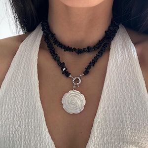 Puede incluir: Un collar de piedras negras de varias capas con un colgante de rosa de concha blanca.