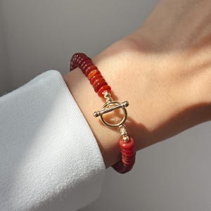 May include: A red and orange beaded bracelet with a gold toggle clasp.