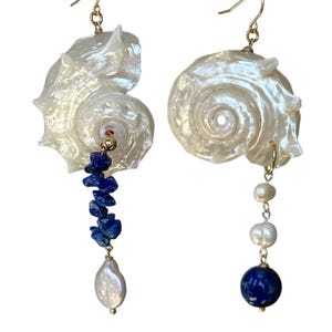 Puede incluir: Un par de pendientes de concha con ganchos dorados. Un pendiente presenta una hebra de virutas de lapislázuli azul y una perla blanca. El otro pendiente tiene perlas blancas y una esfera azul.