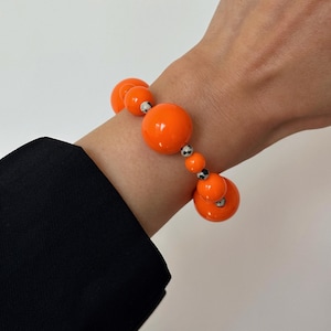 Op de afbeelding: Een feloranje kralenarmband met zwart-wit gevlekte kralen. De armband is gemaakt van grote, ronde kralen.