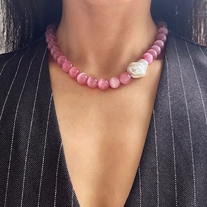 Puede incluir: Una taza de cerámica blanca con un asa negra y el texto "But First, Coffee" en negrita negra. La taza se encuentra sobre un fondo borroso, sugiriendo un ambiente acogedor.