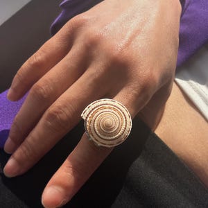 May include: A white seashell ring with brown stripes. The ring is worn on a finger.