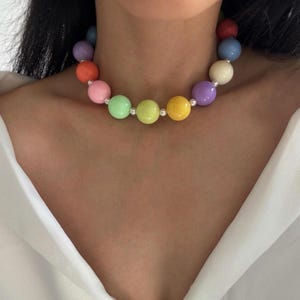 May include: A colorful beaded necklace featuring large, round beads in a variety of pastel colors, including pink, green, yellow, and purple. The beads are strung together with silver-colored connectors, creating a vibrant and playful accessory.