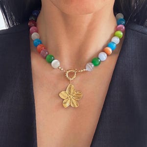 May include: A colourful beaded necklace with a gold flower pendant. The beads are made of various gemstones in shades of green, blue, red, orange, and white.