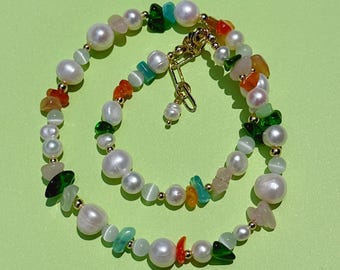 May include: A necklace featuring white freshwater pearls, translucent green and orange stone chips, and small cat's eye beads. The strand is accented with tiny gold-toned metal beads and includes a gold-toned metal lobster claw clasp closure.