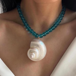 Pode incluir: Um colar de contas azul turquesa com um grande pingente de concha branca.