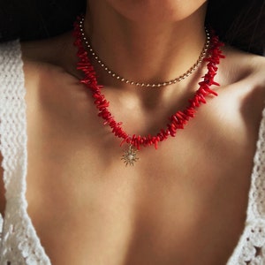 以下が含まれることがあります： 赤い珊瑚のネックレスに金の太陽のペンダントがついたもの。ネックレスは細い金のチェーンの上に重ねられています。