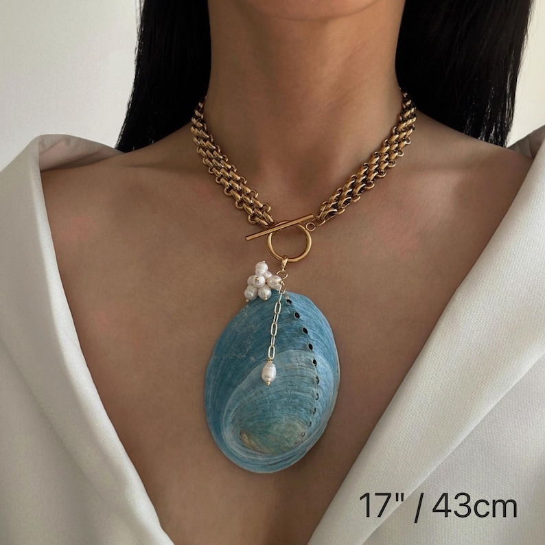 May include: A gold-toned chain necklace featuring a toggle clasp and a large, oval-shaped blue abalone shell pendant. The pendant is accented with a cluster of small white pearls and a single dangling pearl on a delicate chain. Length is 17 inches.