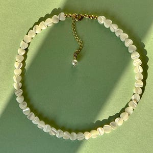 May include: A white heart-shaped bead necklace with a gold chain and a single pearl pendant.