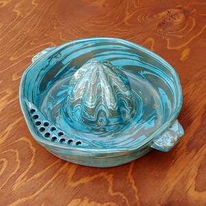 Peut inclure: Un presse-agrumes en céramique bleu et vert avec un motif marbré. Le presse-agrumes a un cône central avec des crêtes et un bord avec de petits trous autour du bord.