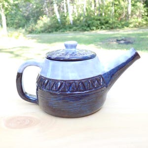 May include: A blue and white ceramic teapot with a geometric pattern around the middle. The teapot has a lid and a spout.