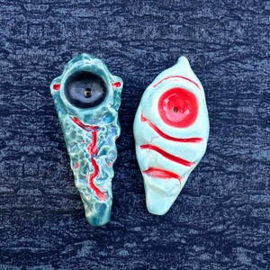 May include: Two ceramic art pieces. One is teal with a black circle and red accents. The other is white with a red circle and red stripes. Both have a hole in the center.