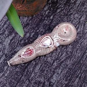 Puede incluir: Un quemador de incienso de cerámica con forma de serpiente estilizada con detalles intrincados y un diseño floral. El quemador está pintado en tonos grises, blancos y rojos.