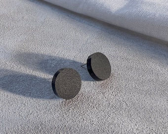 May include: A pair of black round stud earrings. The earrings are made of a smooth, matte material.