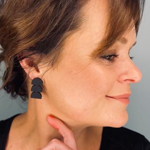 Puede incluir: Pendientes geométricos negros con un diseño de semicírculo en capas. Los pendientes están hechos de un material negro mate y se llevan en la oreja. Los pendientes son de estilo moderno y minimalista.