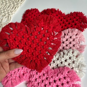 May include: Set of four handmade heart-shaped coasters in red, pink, and white. Each coaster features a fringe border and a woven design.