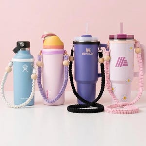 May include: Four water bottles and tumblers in shades of blue, purple, and pink, each with a macrame strap and wooden beads. One has a daisy pattern, another the Aldi logo.