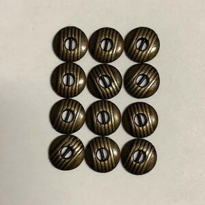 May include: A set of twelve circular metal buttons arranged in a grid. Each button features a dark bronze finish with a series of raised, diagonal parallel lines across the surface and a central horizontal bar spanning the middle opening.