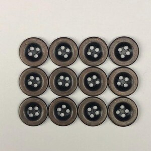 May include: A set of twelve round, dark brown buttons arranged in a grid of three rows and four columns. Each button features a smooth, slightly concave surface with four small holes in the centre for threading, showcasing a uniform finish.
