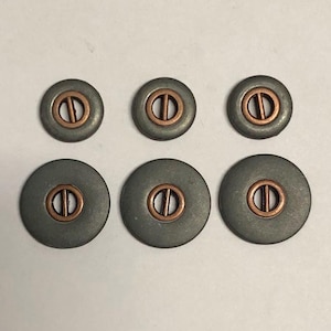 May include: A set of six circular buttons arranged in two rows of three. Each button features a smooth, matte grey outer disc with a centred, circular copper-toned inlay that contains a single vertical bar for threading, creating a contrast.