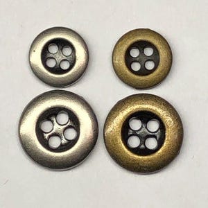 May include: Four round buttons arranged in a square grid. The top two are smaller, while the bottom two are larger. Two buttons are silver-toned with a metallic finish, and two are brass-toned. Each button features four holes in the center.