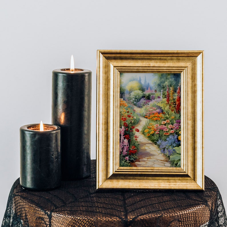 May include: Two black candles with flames and a gold picture frame with a painting of a colorful garden path.