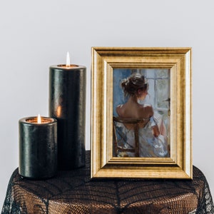 May include: A framed painting of a woman sitting in a chair, facing away from the viewer. The painting is in a gold frame and is on a black lace tablecloth with two black candles.