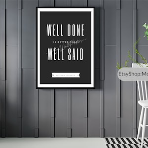 Op de afbeelding: Zwart-witte motiverende quote poster met de tekst "Goed gedaan is beter dan goed gezegd - Benjamin Franklin". De poster is ingelijst en hangt aan een grijze muur.