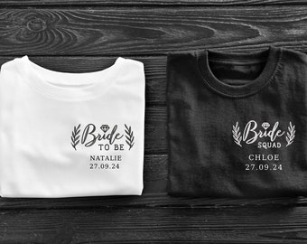 May include: Two white t-shirts with black text. One shirt says "Bride to Be Natalie 27.09.24" and the other says "Bride Squad Chloe 27.09.24".