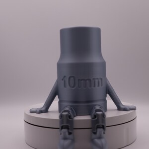 May include: A gray 3D printed figurine of a person sitting with legs outstretched. The figurine has a cylindrical body with the text "10mm" printed on the front.