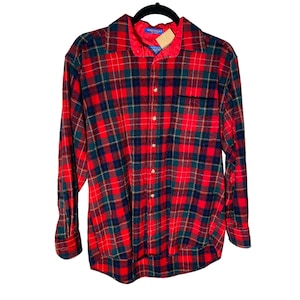 May include: Red, green, and navy plaid flannel shirt with a button-down front, long sleeves, and a chest pocket. The shirt is hanging on a black hanger. The collar has a red lining.