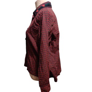 K&ouml;nnte beinhalten: Rot-schwarz kariertes Button-Down-Hemd mit langen &Auml;rmeln. Der Kragen ist dunkelgr&uuml;n mit roter Blumenstickerei. Das Hemd wird auf einer Schaufensterpuppe pr&auml;sentiert, die das Seitenprofil und die Details des Kleidungsst&uuml;cks zeigt.