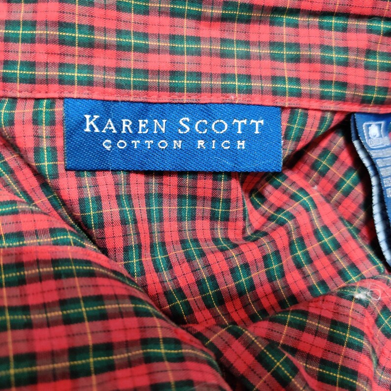 K&ouml;nnte beinhalten: Nahaufnahme eines rot-gr&uuml;n karierten Hemdes. Das Hemd hat ein blaues Etikett mit der Aufschrift "KAREN SCOTT COTTON RICH". Das Karomuster ist ein klassisches Design mit roten, gr&uuml;nen und gelben Linien.