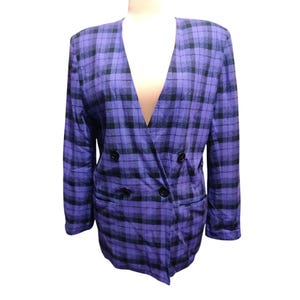 Puede incluir: Un blazer a cuadros morado y negro con un diseño cruzado. El blazer tiene cuello en V y botones negros. La prenda se exhibe en un maniquí.