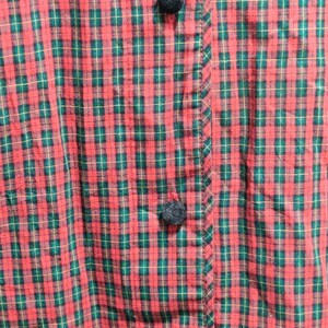 K&ouml;nnte beinhalten: Nahaufnahme eines rot-gr&uuml;nen karierten Stoffes mit Knopfleiste. Der Stoff hat ein klassisches Karomuster mit dunkelgr&uuml;nen und hellbraunen Linien. Die Kn&ouml;pfe sind dunkelgrau.