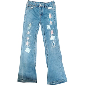 May include: Blue denim jeans with embroidered patches in various colors and patterns.