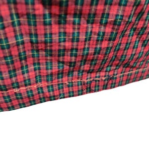 K&ouml;nnte beinhalten: Nahaufnahme eines rot-gr&uuml;nen Stoffes mit Karomuster. Der Stoff hat ein klassisches Karomuster mit einer sichtbaren Naht am unteren Rand. Die Farben sind lebendig und der Stoff scheint leicht strukturiert zu sein.