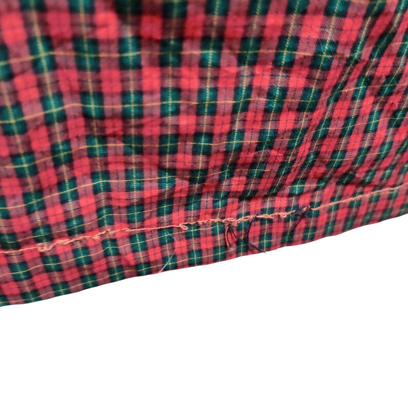 K&ouml;nnte beinhalten: Nahaufnahme eines rot-gr&uuml;nen Stoffes mit Karomuster. Der Stoff hat ein klassisches Karomuster mit einer sichtbaren Naht am unteren Rand. Die Farben sind lebendig und der Stoff scheint leicht strukturiert zu sein.