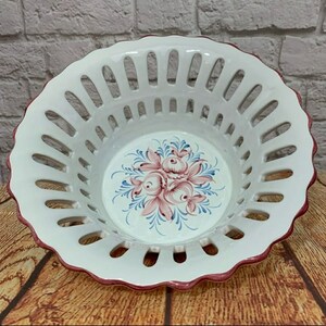 May include: White ceramic bowl with a scalloped edge and a cut-out design. The bowl has a pink and blue floral design in the center.