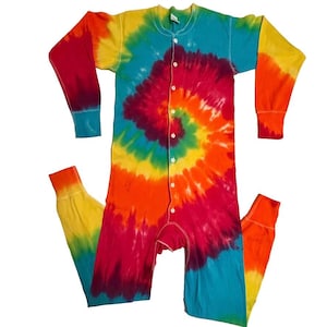 May include: A one-piece, long-sleeved tie-dye pajama set. The colorful garment features a spiral design with hues of red, orange, yellow, green, and blue. It has a button-up front and ribbed cuffs at the wrists and ankles. The pajama set is laid flat.
