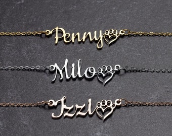 May include: Three delicate necklaces with custom names: "Penny", "Milo", and "Izzi". Each necklace features a cursive name design with a heart and paw print charm. The chains are gold, silver, and bronze.